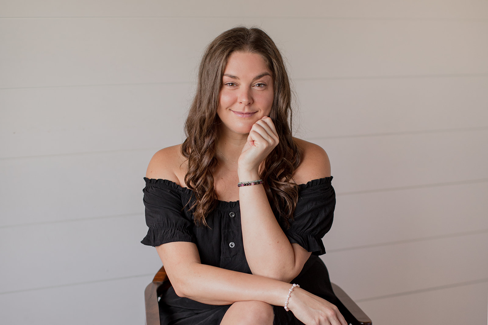 Heather Flynn seated in meditation against a white shiplap wall, hands resting open on her knees